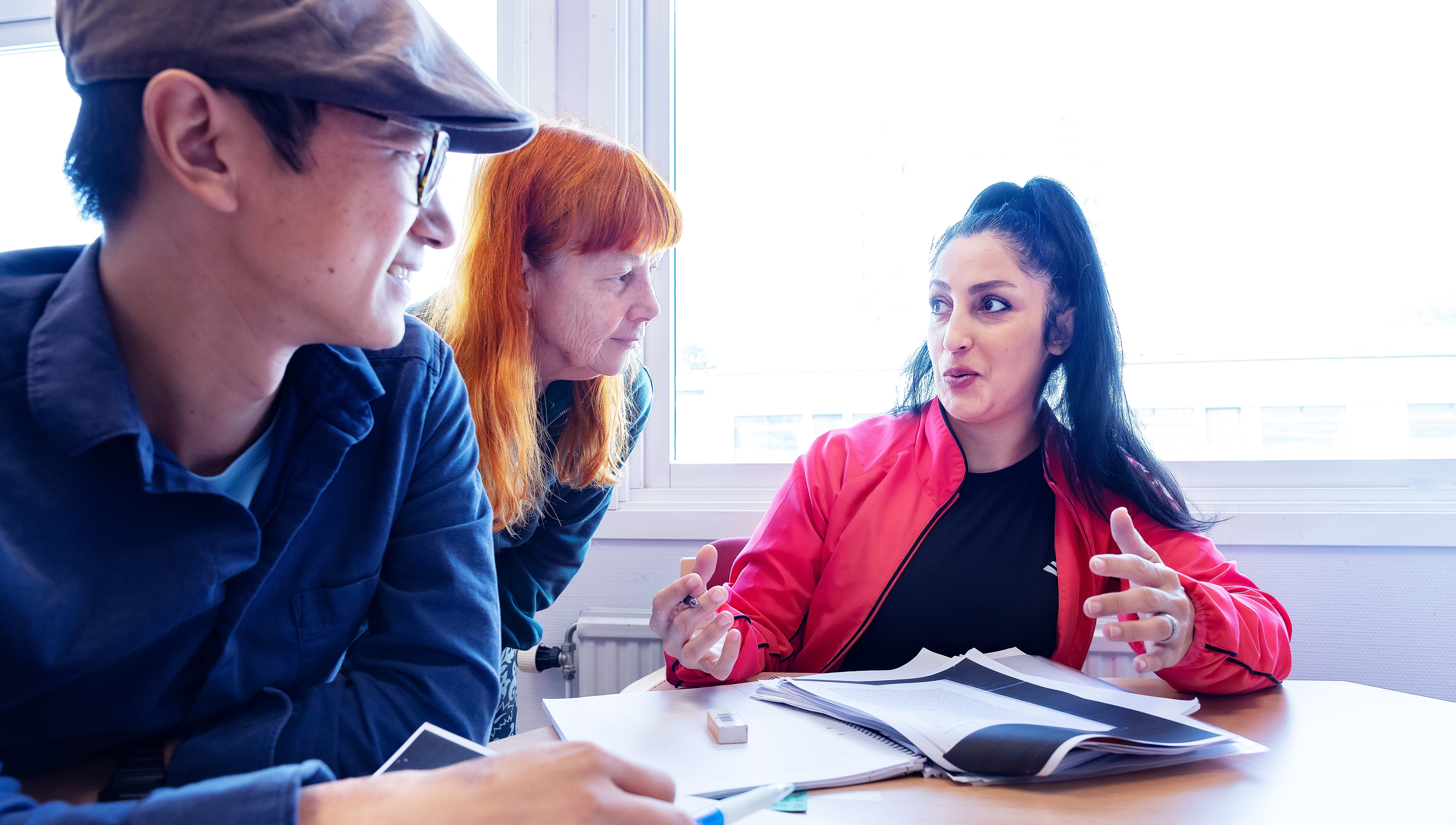Två deltagare vid ett bord får hjälp av en folkhögskolepedagog.