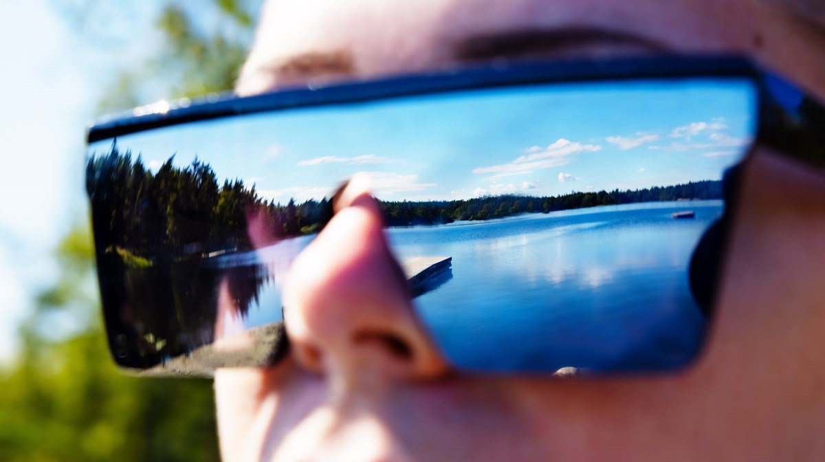 En sjö speglar sig i ett par solglasögon en solig sommardag