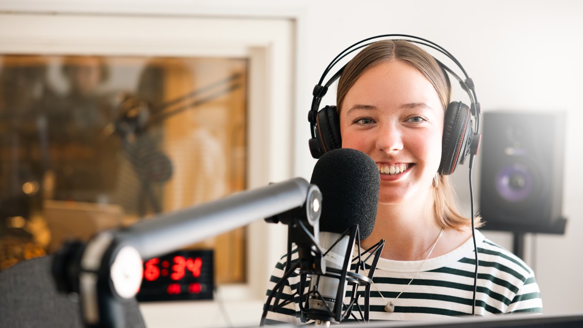 En person står framför en mikrofon i en radiostudio och ler